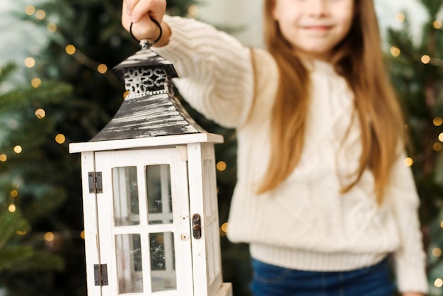 Cute baby girl holding a christmas lantern among the christmas trees