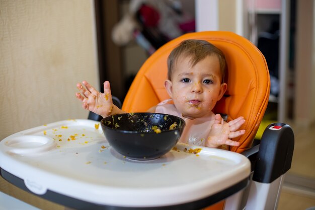 Фото Милая девочка в детском сиденье с едой вскидывает руки и смотрит в камеру в еде