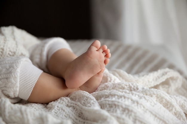 Милые ноги ребёнка на белом одеяле на естественном свете в селективном фокусе