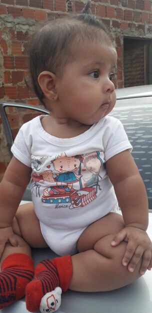 Photo cute baby girl looking away while sitting outdoors