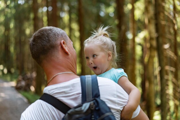 cute baby girl making funny face on father hands.Man with backpack carry daughter in forest. High quality photo