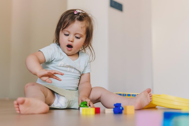 Cute baby girl playing with colorful blocks sitting on a floor at home Baby development Educational toys for young children Construction block for baby or toddler kid