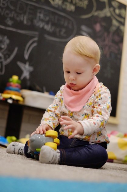 Photo cute baby girl playing with toys while sitting on rug at home