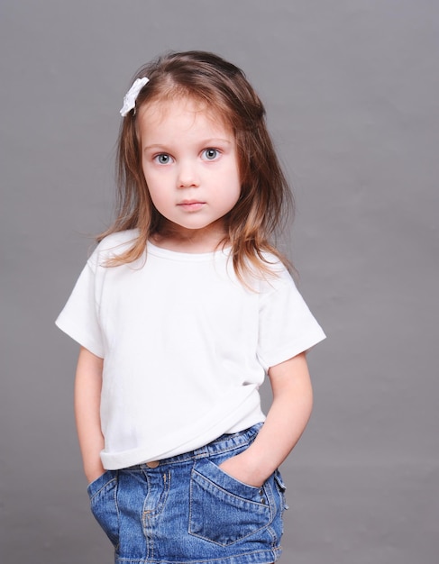 Cute baby girl posing in studio wearing jeans skirt and white shirt Looking at camera