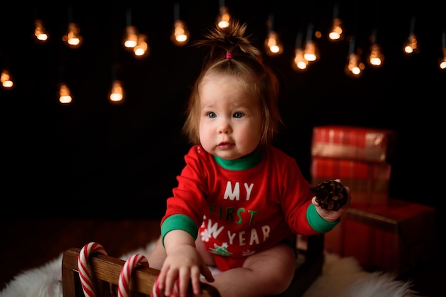 Cute baby girl in a red Christmas costume with retro garlands sits on a fur