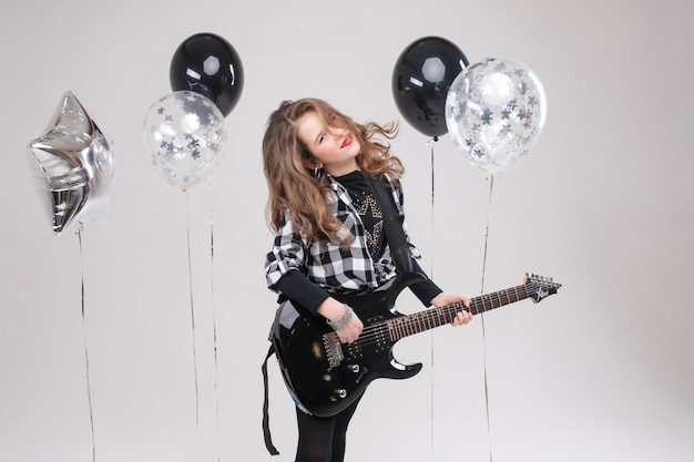 Cute baby girl rock star playing electric guitar and singing song surrounded by balloons