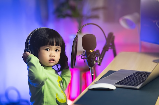 Foto bambina carina che canta con le cuffie registrando una nuova canzone con il microfono nello studio di registrazione domestico