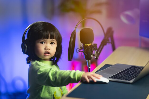 Cute baby girl singing with headphone recording new song with\
microphone in the home recording studio