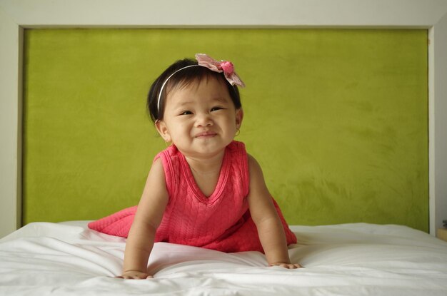 Cute baby girl sitting on bed against wall at home