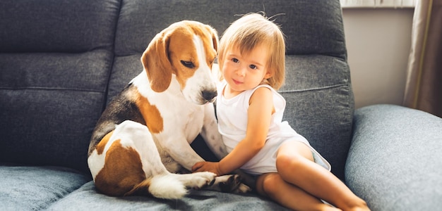 Photo cute baby girl sitting with dog on sofa at home