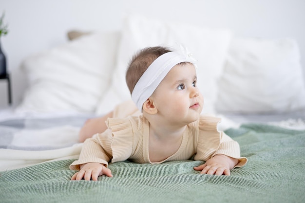 6개월 된 귀여운 여자 아기는 행복한 신생아 집에 있는 녹색 침대를 바라보고 있습니다