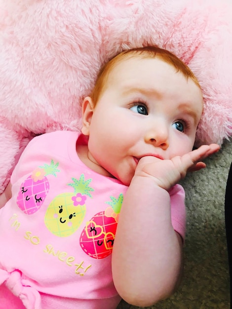 Photo cute baby girl sucking thumb while lying on bed at home