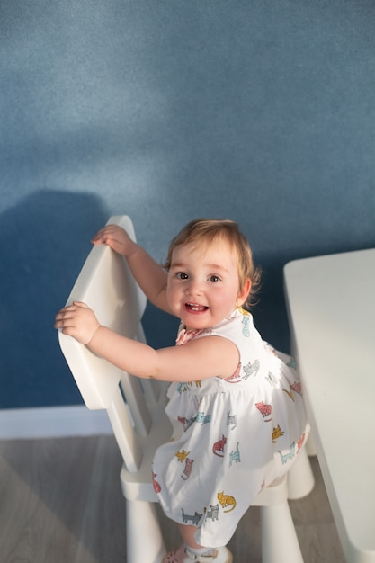 Cute baby girl wearing dress sitting on chair and looking at camera. vertical format, copy space