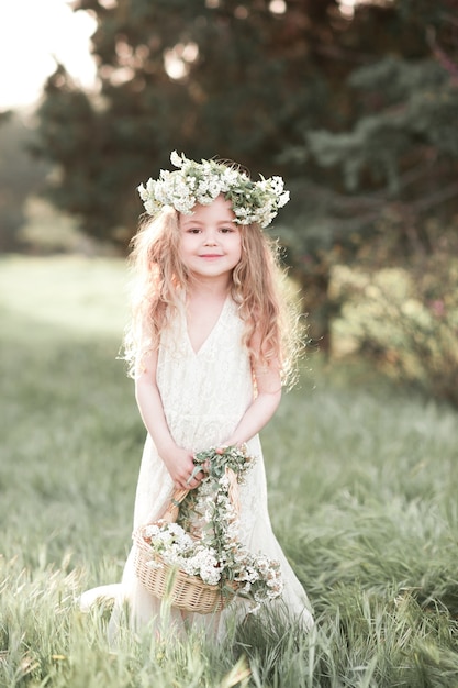 Cute baby girl wearing white dress and floral wreath outdoors