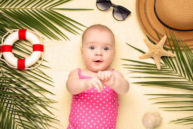 Cute baby girl with beach accessories on light background. Holidays at sea with baby, summer concept