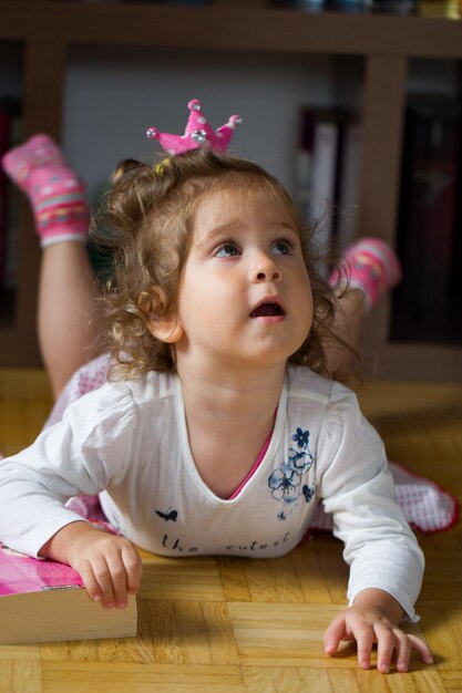 Cute baby girl with book lying on hardwood floor