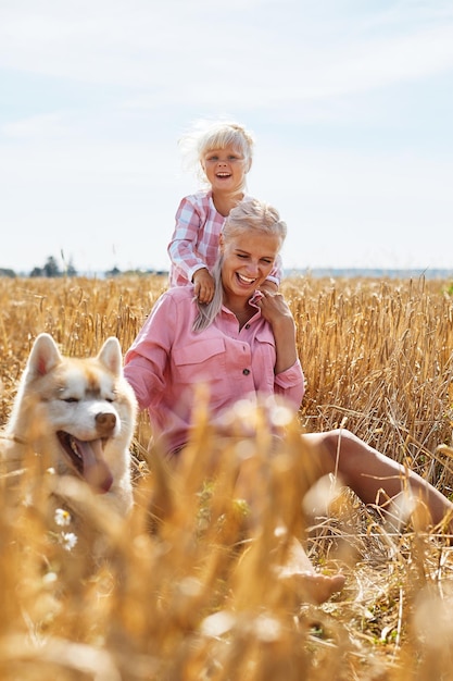 Photo cute baby girl with mom and dog on wheat field happy young family enjoy time together at the nature