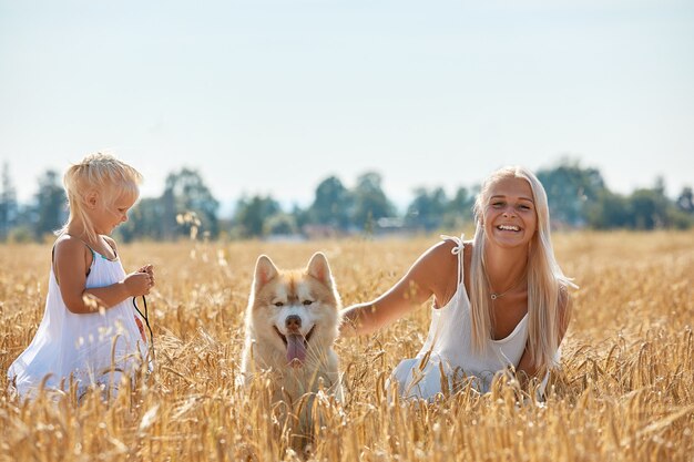 Cute baby girl with mom and dog on wheat field