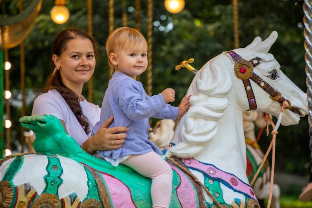 Photo cute baby girl with mother on the horse of old retro carousel prague czech republic