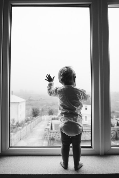 Cute baby at home in white room stands near window