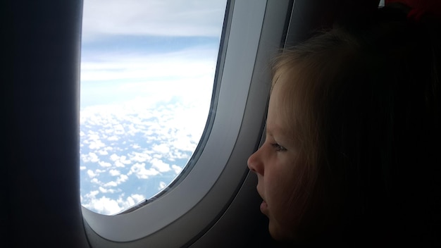 Cute baby is looking at airplane window and concept of first flight journey with kids