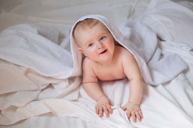 귀여운 아기가 흰색 면 침구가 깔린 침대에 기저귀를 하고 누워 있습니다. 고품질 사진