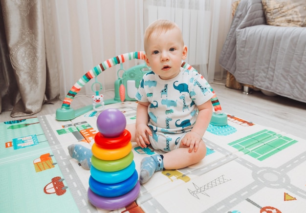 A cute baby is playing with a rainbow toy pyramid while sitting on a play mat in a sunny bedroom Toys for small children