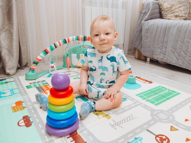 A cute baby is playing with a rainbow toy pyramid while sitting on a play mat in a sunny bedroom Toys for small children