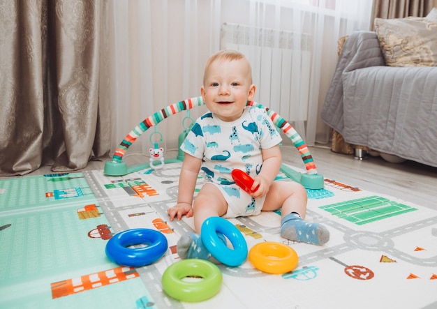 A cute baby is playing with a rainbow toy pyramid while sitting on a play mat in a sunny bedroom Toys for small children