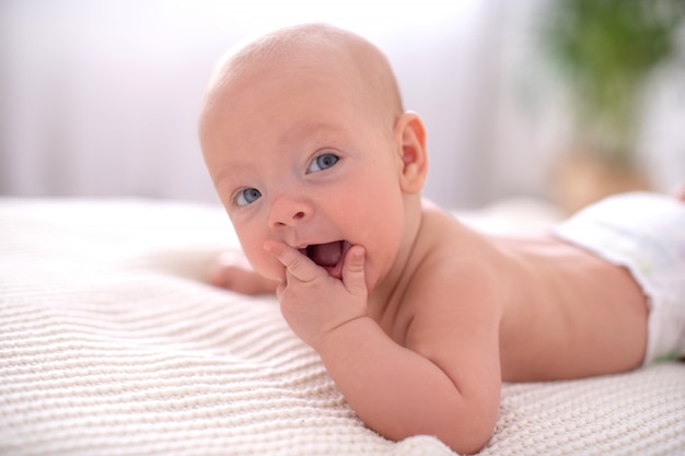 Il bambino sveglio si trova sul suo stomaco per strisciare e tiene la sua mano nella sua bocca. dentizione