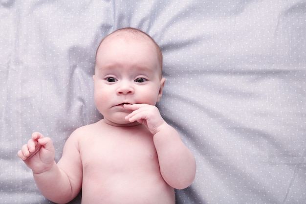 Cute baby lying with her fingers in mouth, top view