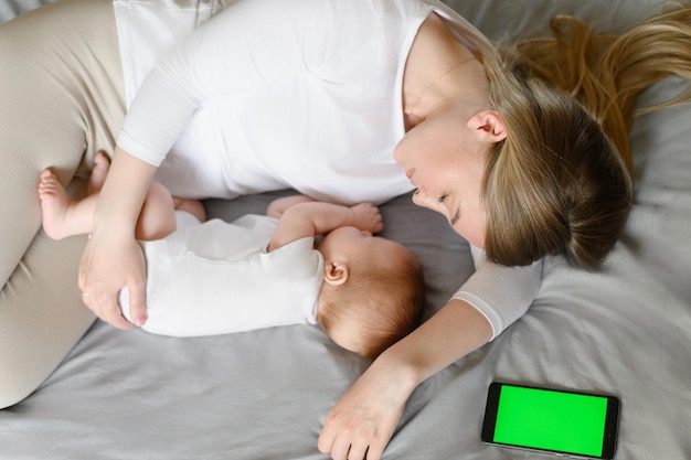 Cute baby and mother hugging sleep at home in bed next to phone color key child safety and protectio