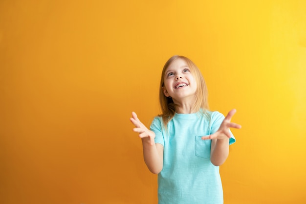 Cute baby on an orange wall, 6-8 years old, baby girl catches something or is ready to catch falling from above