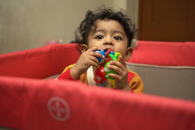 Cute baby playing in a playpen with teething toys in its mouth