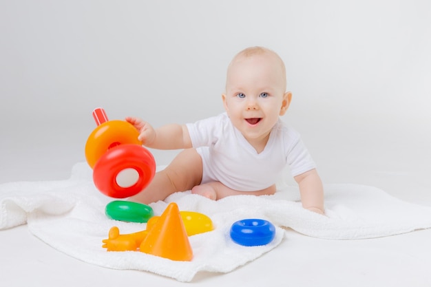 Cute baby playing with colorful rainbow toy pyramid sitting on white backgroundToys for little kids