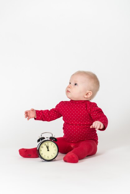 Cute baby in red outfit playing with a clock