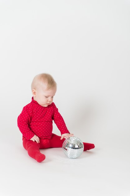 Cute baby in red outfit playing with a party ball