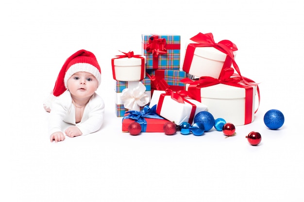 Cute baby in a red Santa Claus cap with christmas gifts
