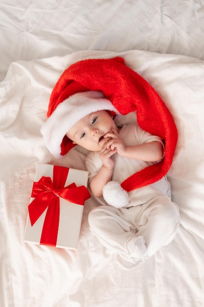 自宅のベッドでサンタ帽子をかぶったかわいい赤ちゃん。最初の新年。クリスマスギフト