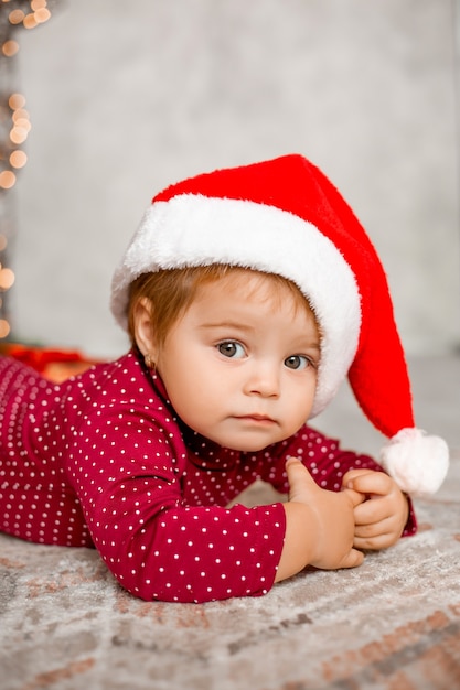 Cute baby Santa sits at home near the Christmas tree with gifts