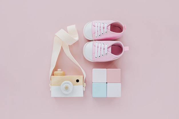 Scarpe da bambino carine con macchina fotografica giocattolo in legno e blocchi colorati. set di cose per bambini e accessori per ragazza su sfondo rosa pastello. concetto di doccia per bambini. moda neonato. disposizione piatta, vista dall'alto