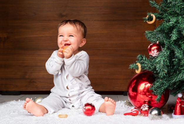귀여운 아기는 크리스마스 트리 근처 바닥에 앉아