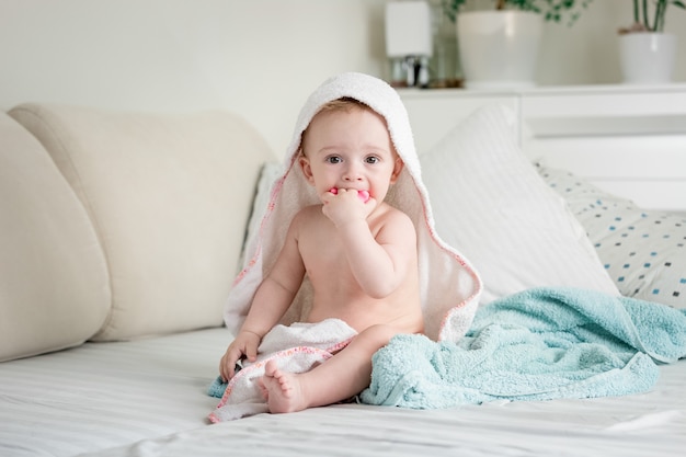 Cute baby sitting on bed covered in towels