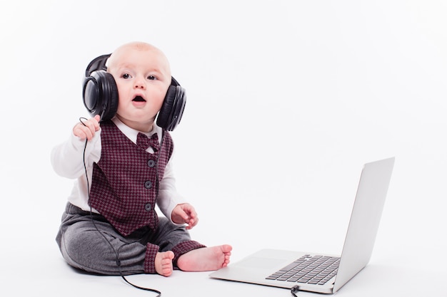 Cute baby sitting in front of a laptop wearing headphones