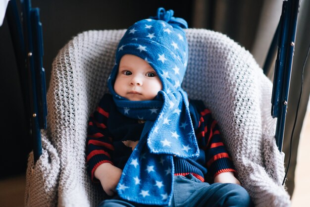 Cute baby sitting in a high chair in blue hat and scarf, swings