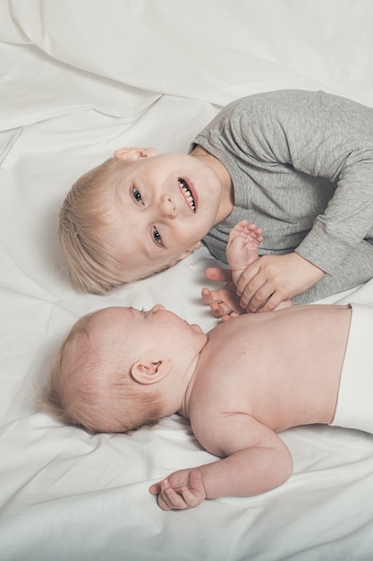 Cute baby and smiling older brother lying on the bed