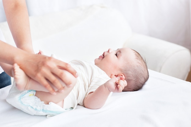 Cute baby sorridente mentre sua madre sta cambiando il pannolino in camera da letto