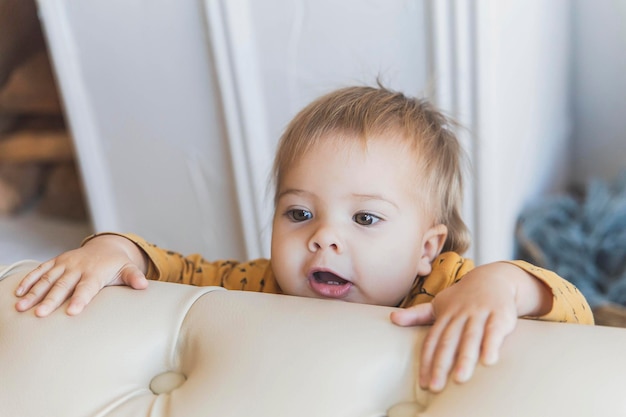 Cute baby trying to get out on the sofa and smiles so that two teeth are visible