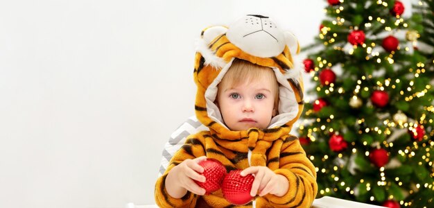 Cute baby wearing costume of tiger symbol of new 2022 year indoor near of christmas treeCopy space