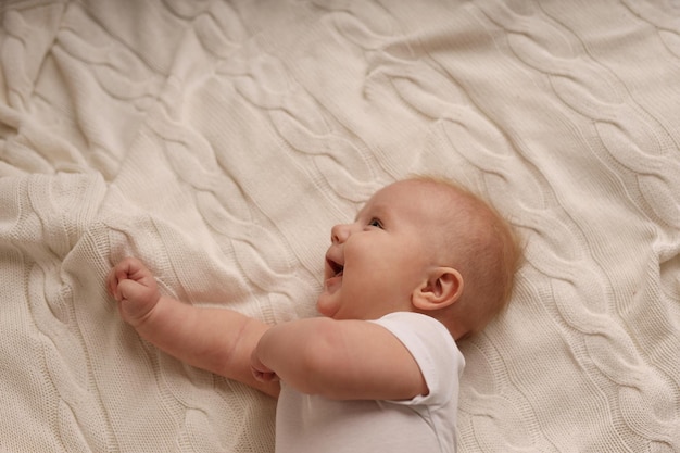 cute baby in a white bodysuit lying on a white bedspread